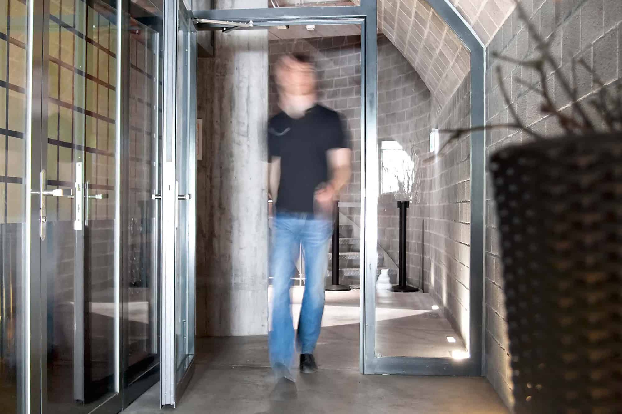 Persoană care trece printr-o ușă automată multimarcă în interiorul unui spațiu modern.
